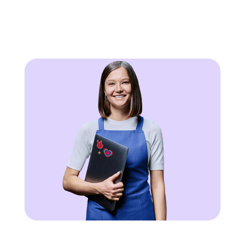 Smiling young woman in blue apron holding decorated laptop against purple background