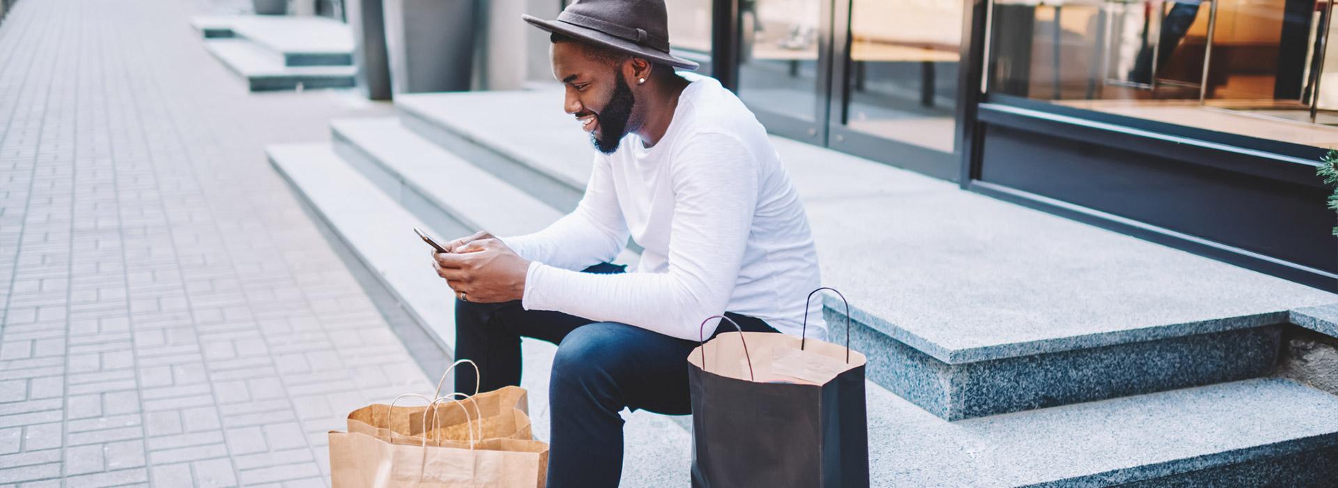 man sitting on steps with shopping bags holding cell phone