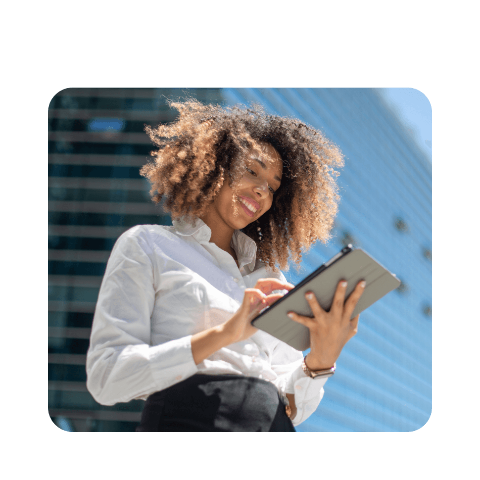 Woman with curly hair in white shirt holding tablet outdoors against blue sky and building